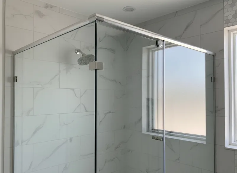 Close-up detail shot of a semi-frameless shower enclosure header and top framing channel, showing brushed nickel or chrome...