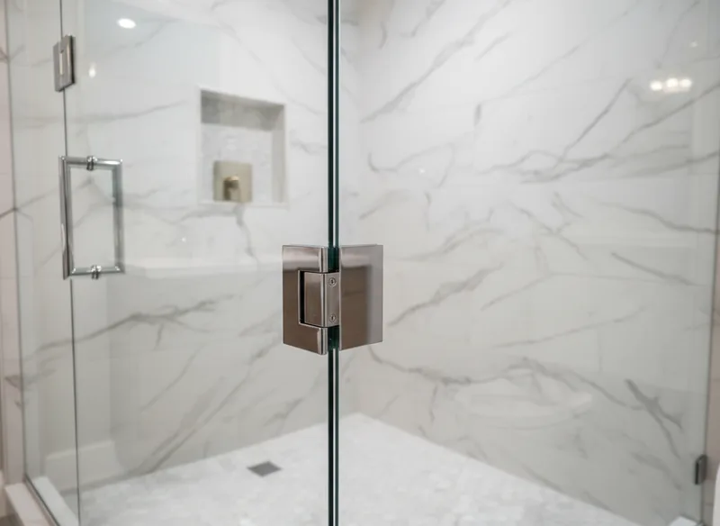 Close-up detail shot of the corner junction where frameless glass panels meet chrome hinges and handles, showing the preci...