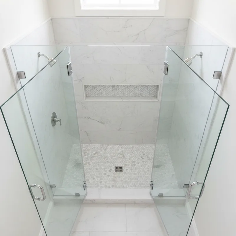 An overhead shot of a spacious walk-in shower enclosure with frameless glass doors open, showing the interior tile work an...