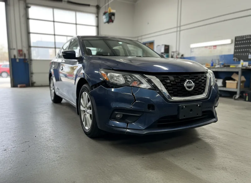 Wide-angle view of a vehicle with visible bumper damage from a frontal collision, showing cracking and misalignment, photo...
