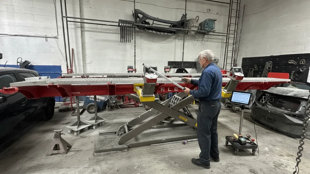 Certified technician inspecting a vehicle frame on an alignment rack with precision measuring equipment in a professional aut