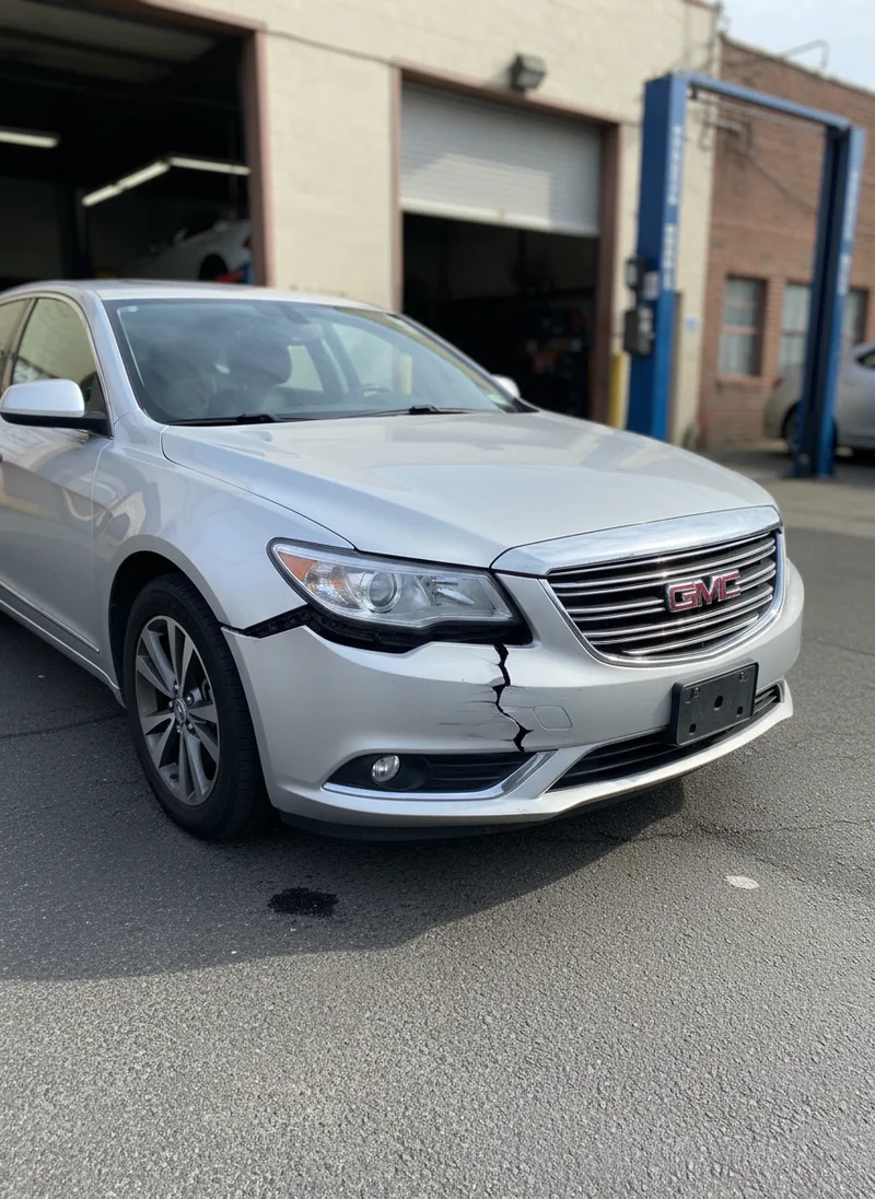 Wide-angle photograph of a vehicle with visible bumper damage including dents, cracks, and misalignment, parked in dayligh...