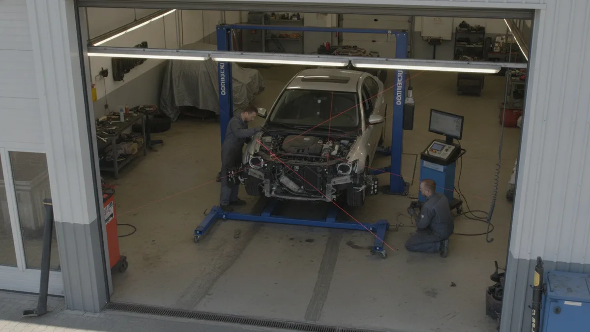 Technician inspecting a vehicle on a frame alignment rack in a collision repair shop.